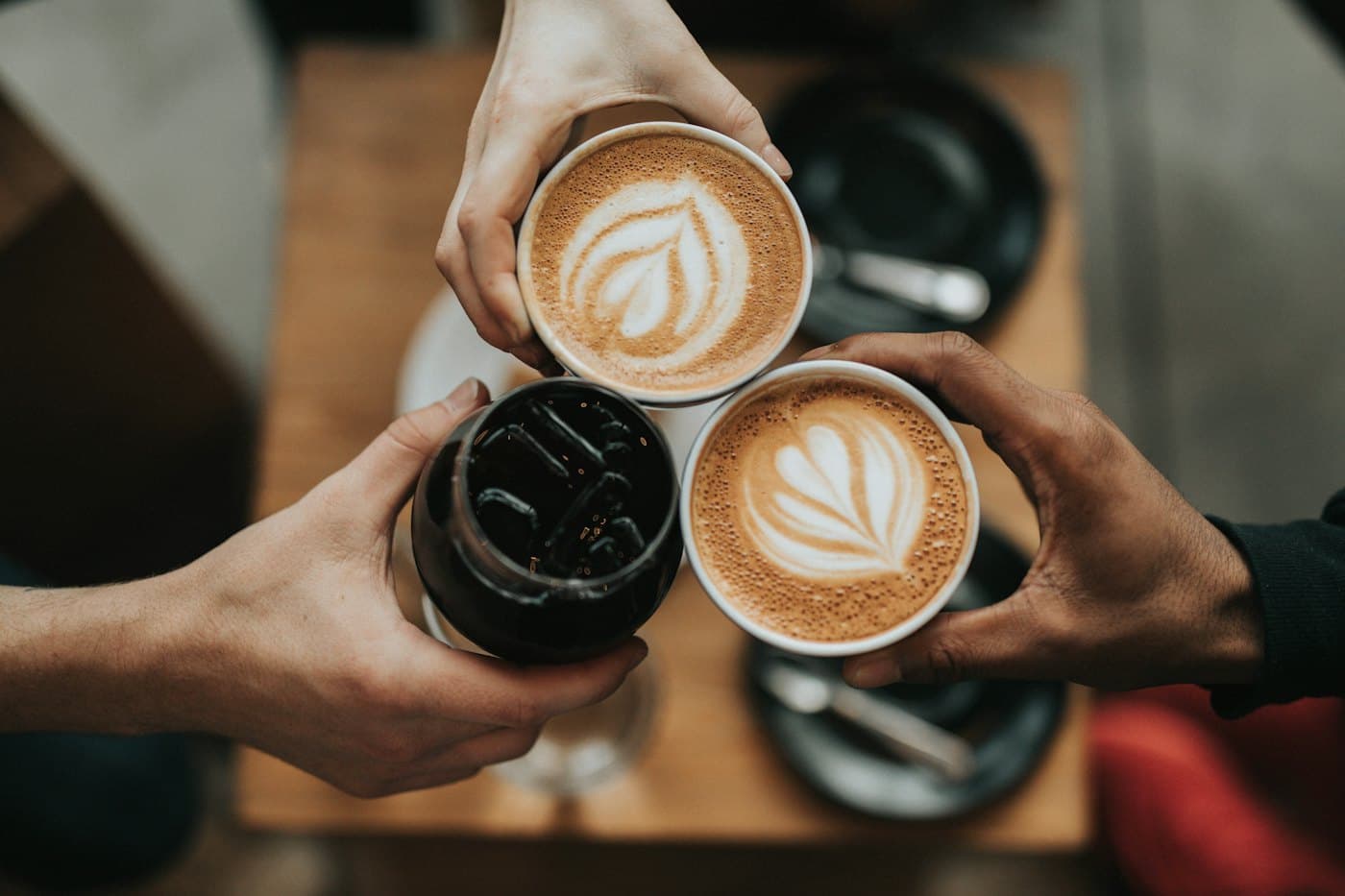 Three people raising coffee drinks together